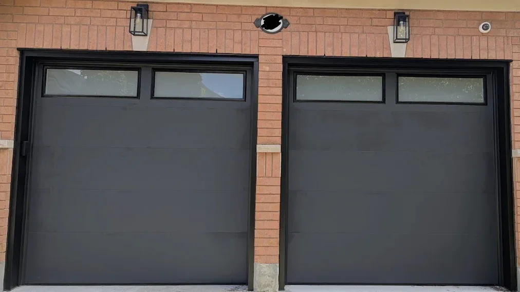 Two completed black garage doors on a brick home